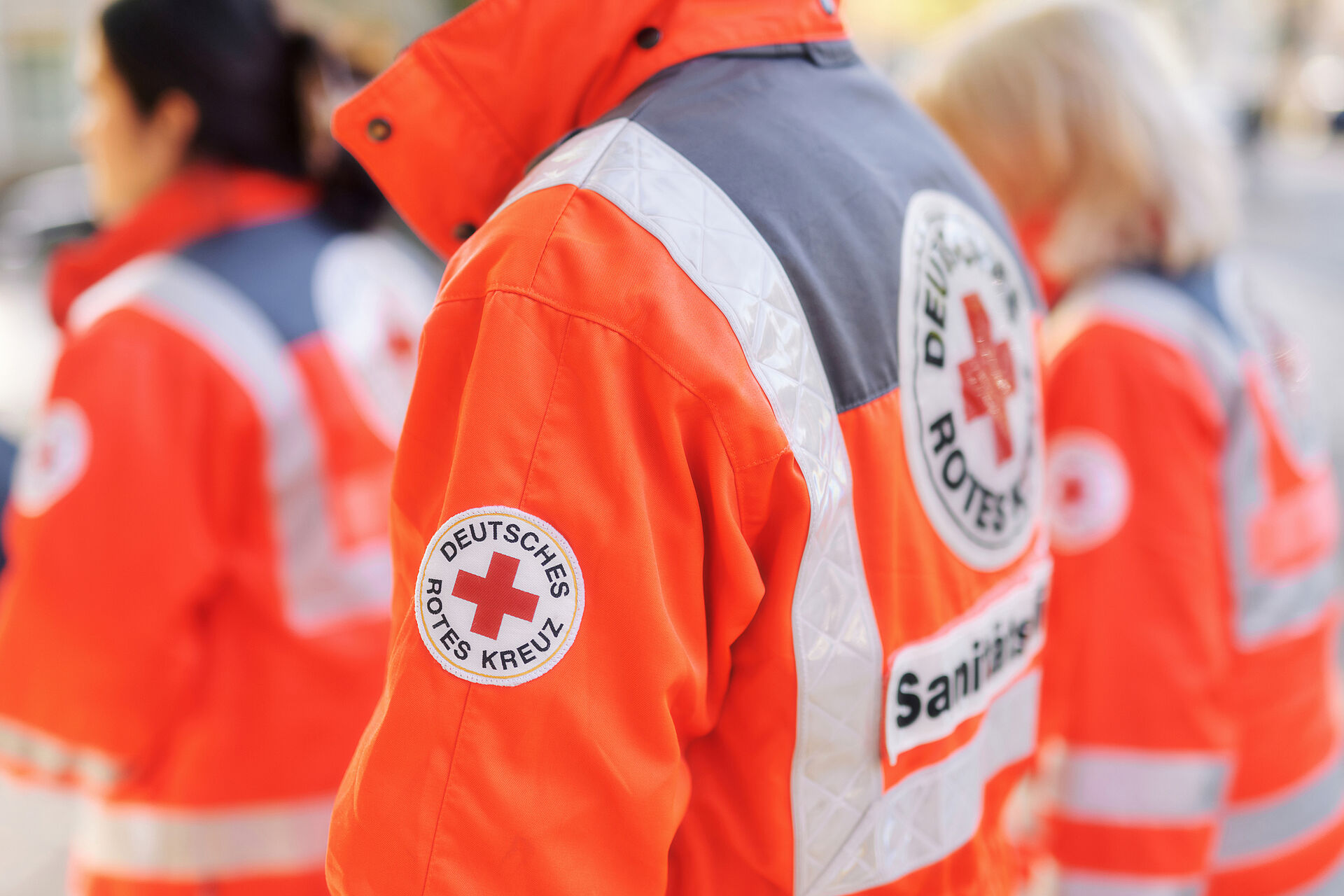 Sanitätsdienst Drei Personen in roter DRK-Einsatzkleidung stehen nebeneinander mit dem Rücken zur Kamera.