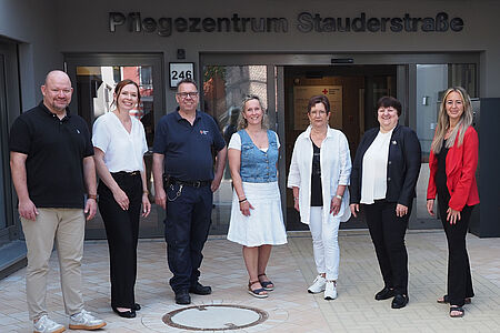 Acht Personen stehen in einem Halbkreis nebeneinander vor der Eingangstür des DRK-Pflegezentrums Stauderstraße.