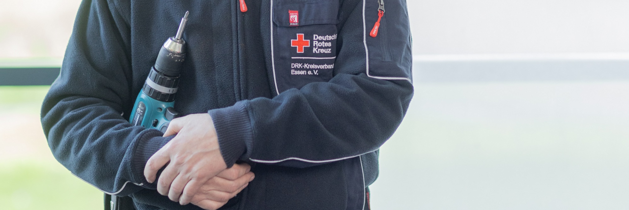 Ein ehrenamtlicher Heinzelwerker des DRK Essen hält einen Akkuschrauber in den Händen und lächelt in die Kamera.