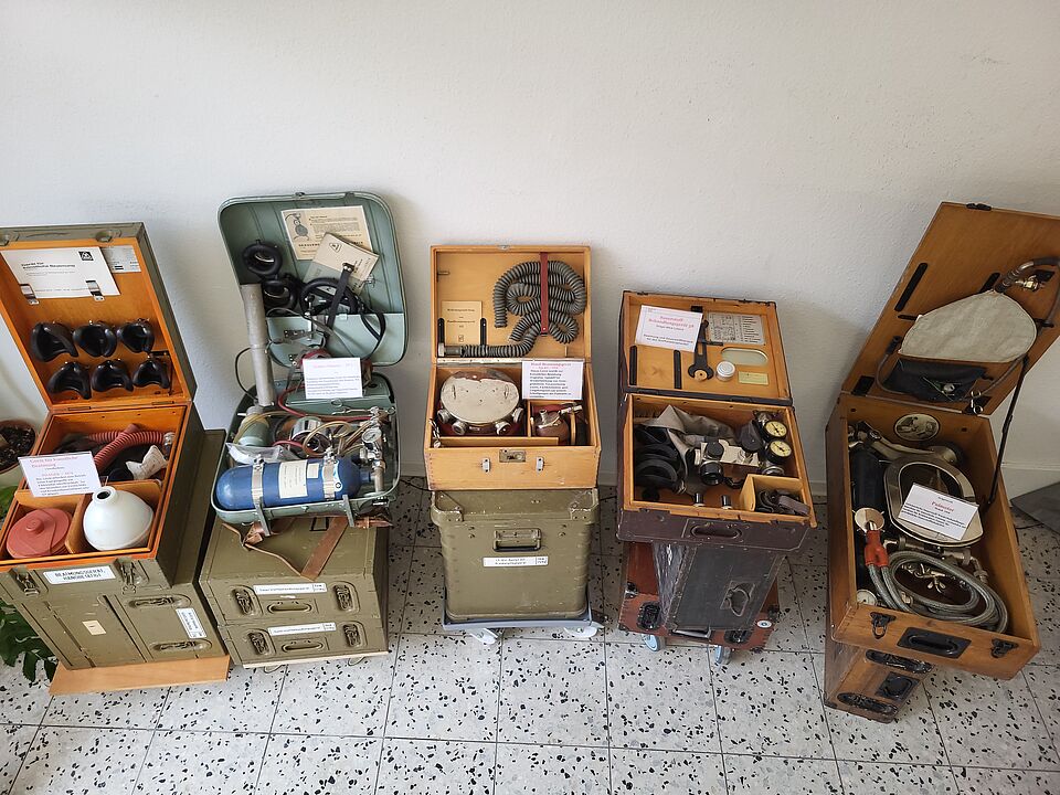 Mehrere geöffnete historische Transportkoffer mit medizinischen Geräten, Schläuchen, Masken und weiterer Sanitätsausrüstung.