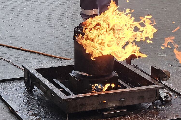 Kurs zum Brandschutzhelfer Mensch steht in Schutzkleidung hinter einem Feuerkorb.