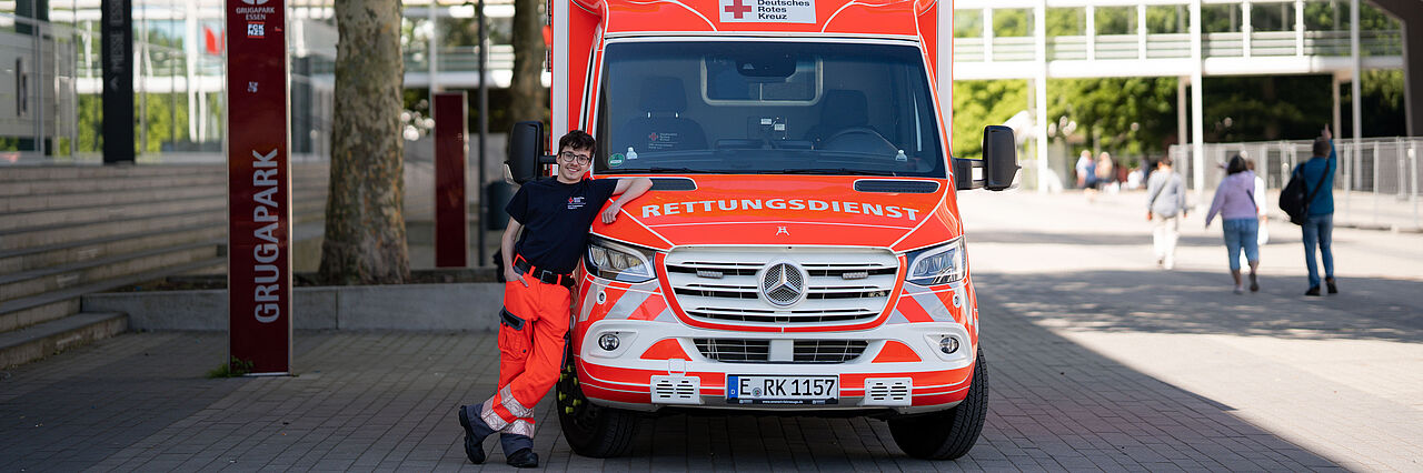 Ein junger Mann in Dienstkleidung lehnt an einem Rettungswagen.