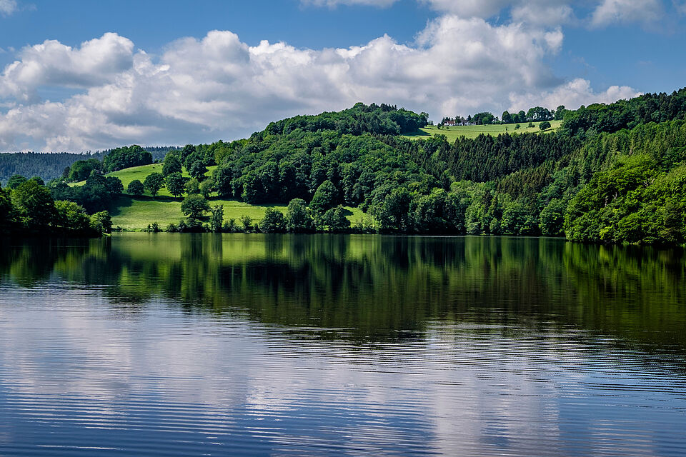 Seniorenreisen Dunkelblauer See mit grünen Wiesen im Hintergrund