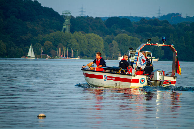 Boot der Wasserwacht fährt im Sonnenuntergang auf dem Wasser, zwei Personen sind an Board.