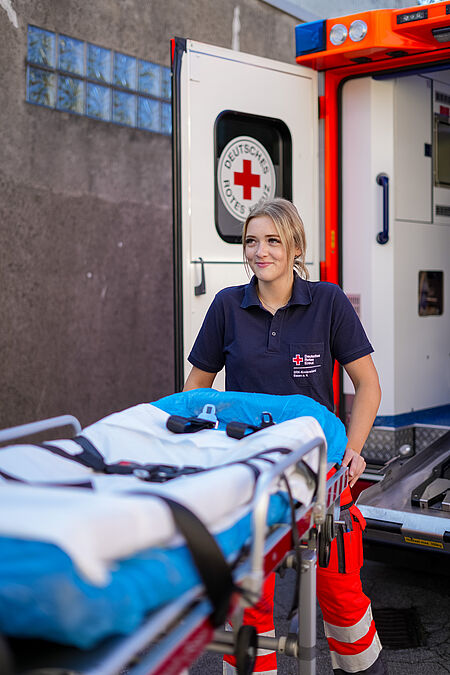 Eine Rettungssanitäterin schiebt die Trage aus dem Rettungswagen heraus.