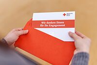 Jemand zieht eine Karte aus einem Umschlag. Darauf steht "Wir danken Ihnen für Ihr Engagement".
