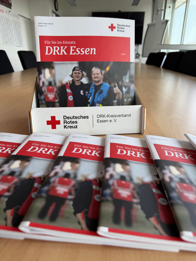 Aktuelle Ausgabe der DRK Essen-Broschüre „Für Sie im Einsatz.“ in einem Aufsteller auf einem Konferenztisch, umgeben von mehreren ausliegenden Exemplaren.