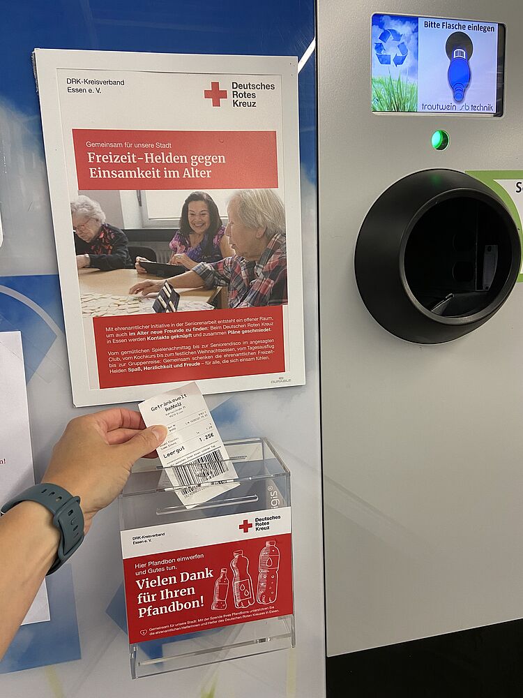Unternehmenskooperation Pfandbon An einem Pfandautomaten wird ein Pfandbon in eine Spendenbox gesteckt.