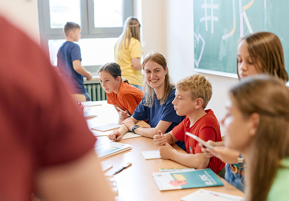 Mehrere Kinder sitzen in einer Schulklasse vor Broschüren und Flyern des JRK.