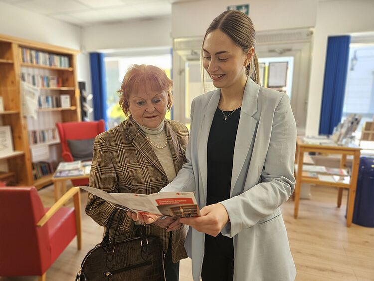Zentrum 60plus Heckstraße Jüngere und ältere Frau schauen sich im Zentrum 60plus Heckstraße zusammen stehend eine Broschüre an.