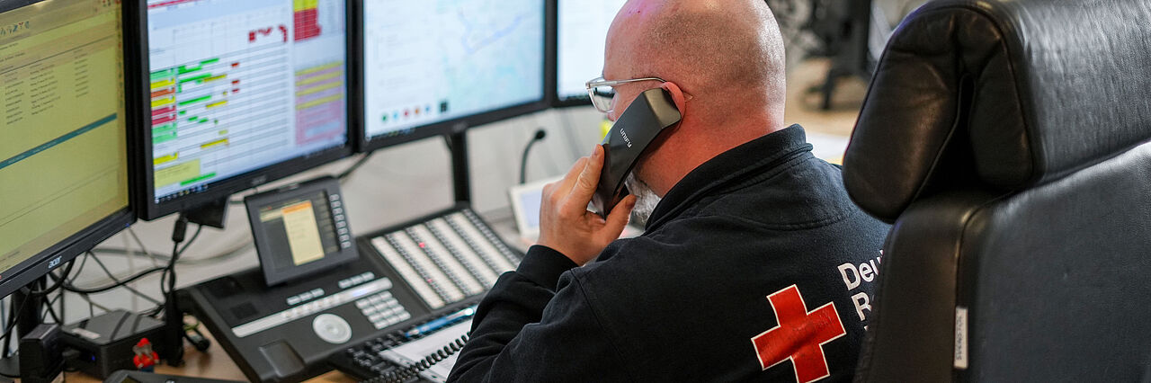 Ein Mann des DRK Essen sitzt in der Einsatzleitzentrale vor mehreren Monitoren und telefoniert.