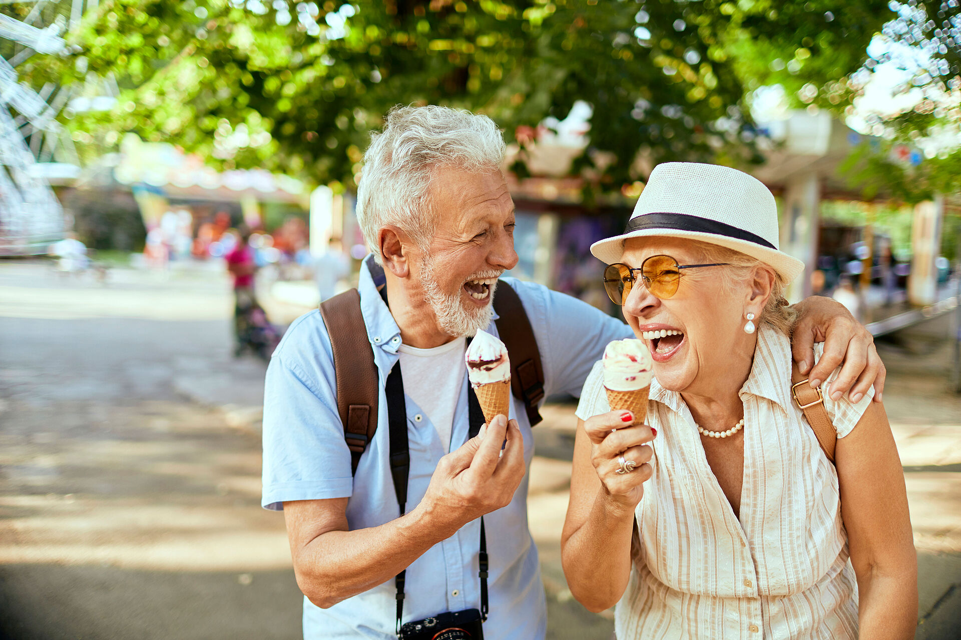 Seniorenreisen Zwei ältere Menschen essen lachend ein Eis und halten sich dabei im Arm.