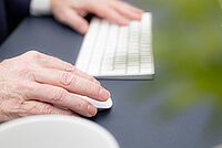 Hände bedienen eine weiße Computer-Tastatur und Maus