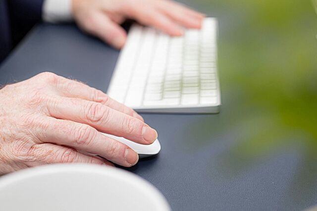Hände bedienen eine weiße Computer-Tastatur und Maus