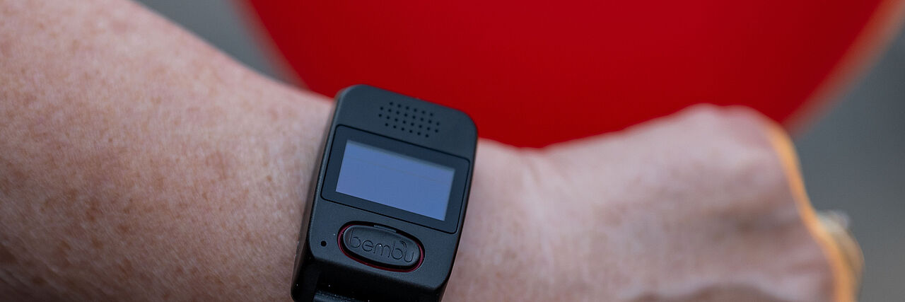 Handgelenk mit DRK-Smartwatch im Hintergrund ist ein roter Ballon mit DRK-Logo