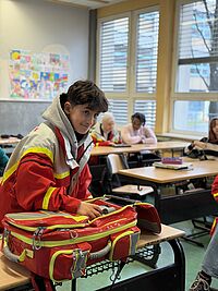 Ein Schüler in JRK-Einsatzkleidung bestückt im Klassenzimmer den Notfallrucksack
