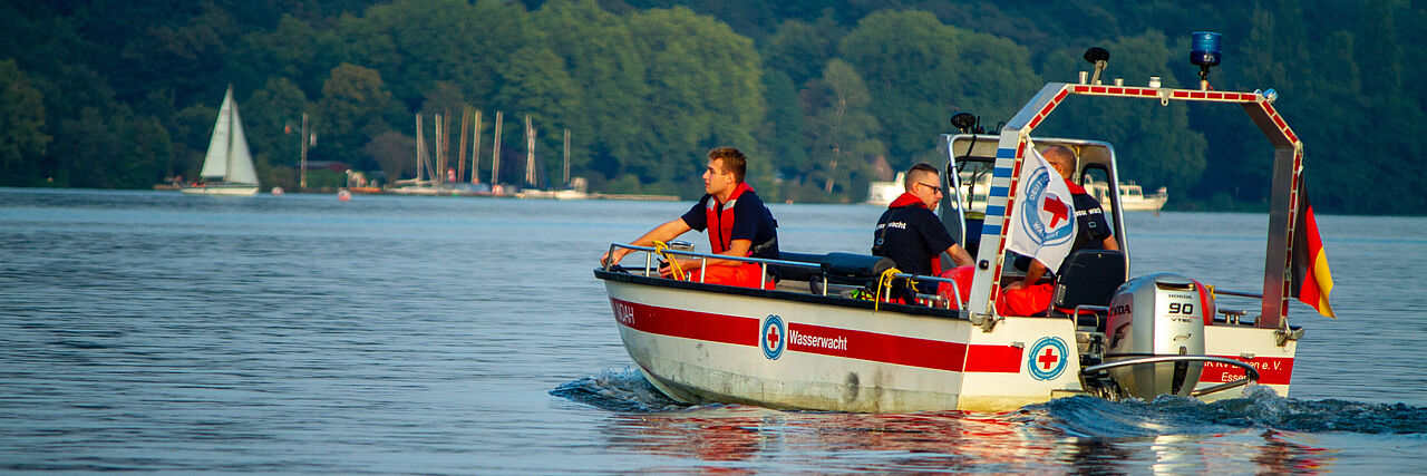 Boot der Wasserwacht fährt im Sonnenuntergang auf dem Wasser, zwei Personen sind an Board.