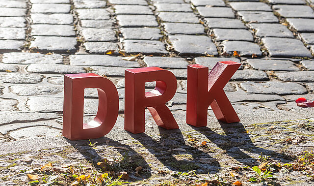 DRK als rote Buchstaben stehen auf einem Kopfsteinpflaster.