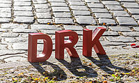 DRK als rote Buchstaben stehen auf einem Kopfsteinpflaster.