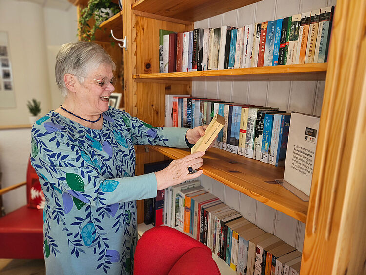 Zentrum 60plus Heckstraße Ältere Frau schaut sich ein Buch aus nebenstehendem Bücherregal an.