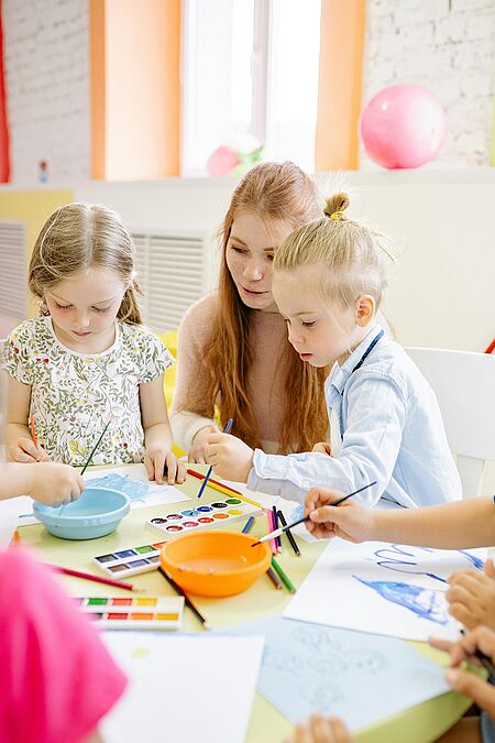 Eine Frau und zwei Kinder malen mit Aquarellfarben.