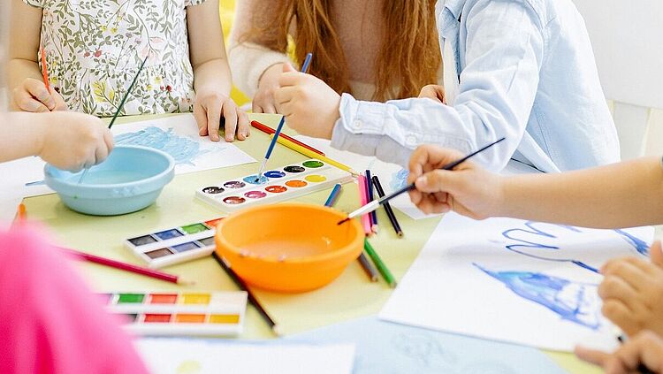 Eine Frau und zwei Kinder malen mit Aquarellfarben.