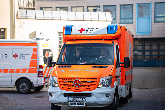 Ein Rettungswagen des DRK Essen fährt los mit Blaulicht. Im Hintergrund sind Gebäude sichtbar.